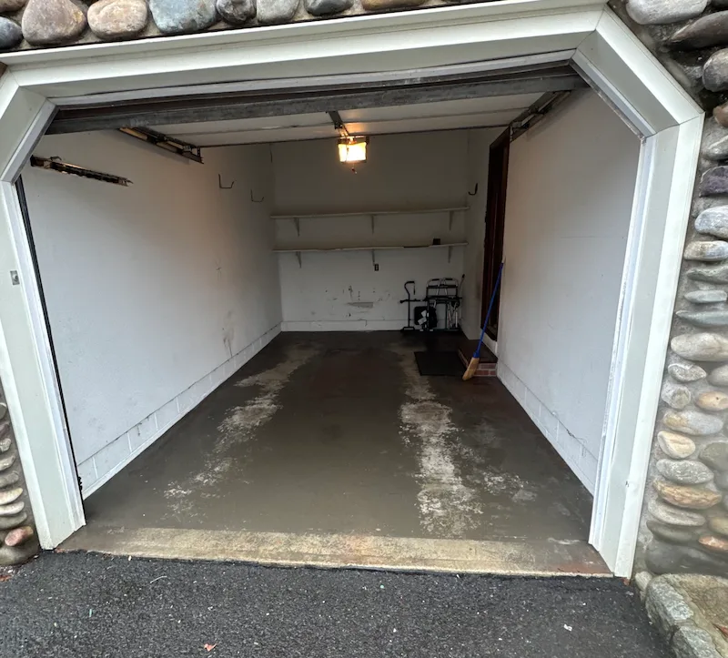 A completely cleared and swept attached garage in North Jersey, showing a clean concrete floor and empty shelving after professional junk removal.
