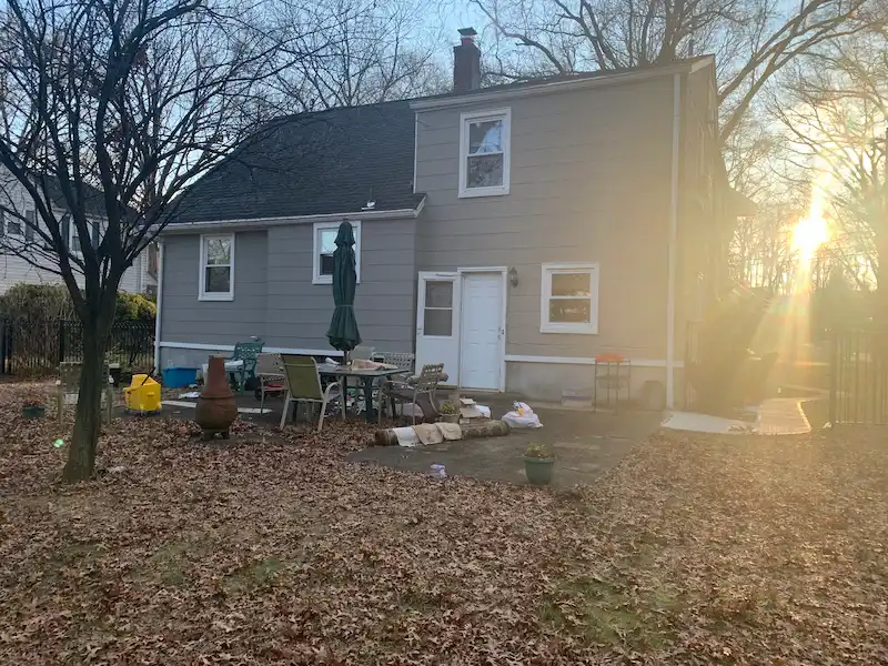 Before photo: A cluttered residential backyard patio in New Jersey filled with old outdoor furniture, a fire pit, and random debris before a professional yard cleanup.