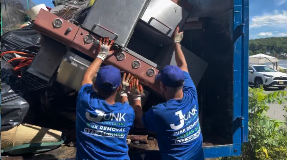 Junk Doctors NJ crew member moving a large stainless steel gas grill for removal and hauling from a residential driveway.