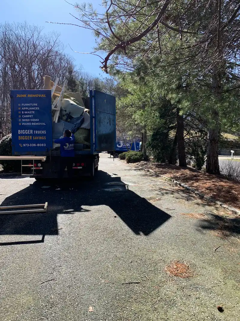 Junk Doctors NJ team loading rolled-up old carpet and padding into a large junk removal truck for proper disposal and recycling.