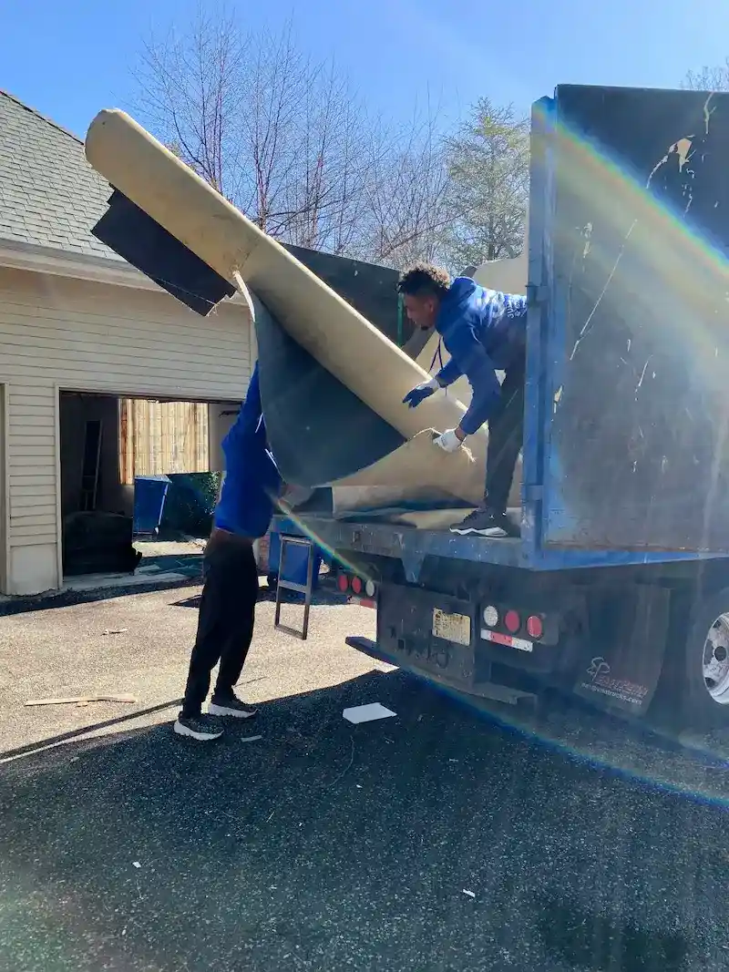 Junk Doctors NJ team members loading old rolled-up carpet and padding into a truck for professional hauling and disposal in North NJ.