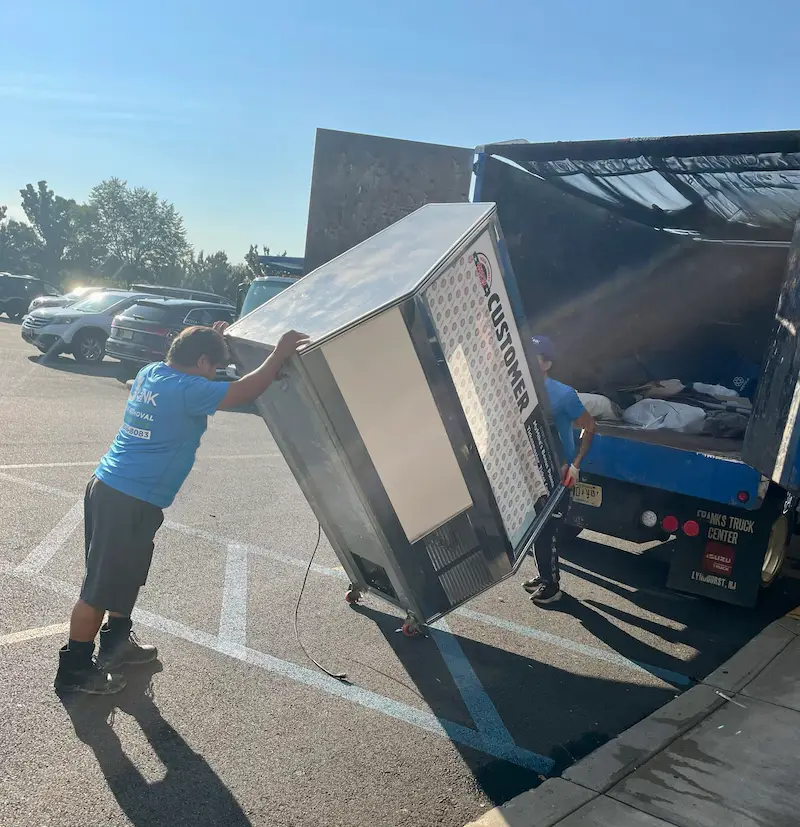 Junk Doctors NJ crew members carefully loading a heavy commercial refrigeration unit during a retail store cleanout project in North Jersey.