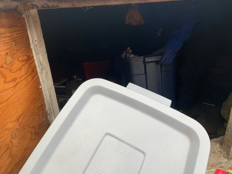 A JunkDoctors team member removing heavy storage bins from a tight residential crawl space during a cleanout in New Jersey.