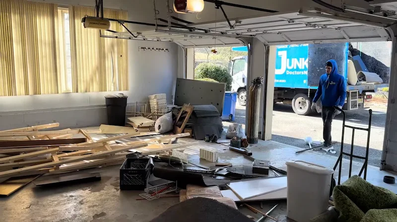 Junk Doctors NJ team member clearing out a cluttered garage filled with wood scraps and household debris during an emergency residential cleanout.