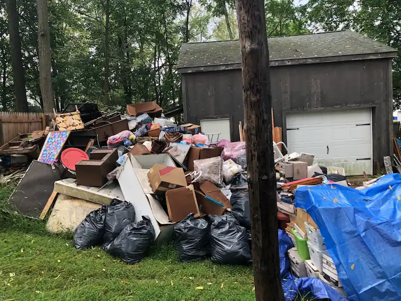 A massive exterior hoarding pile consisting of furniture, boxes, and debris staged for removal in a New Jersey backyard.
