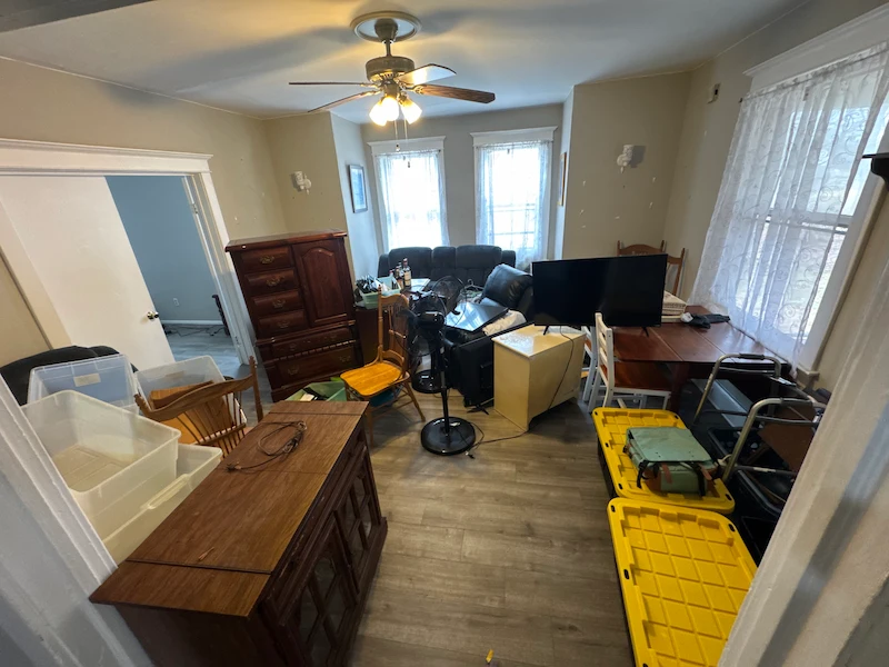 Cluttered living room before professional junk removal, featuring old furniture, TVs, and storage bins ready for disposal.