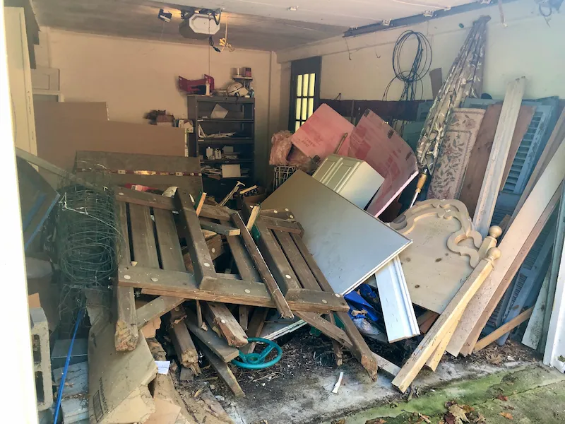 A cluttered garage in North Jersey filled with scrap wood, insulation, rugs, fencing, and old furniture before a Junk Doctors cleanout.