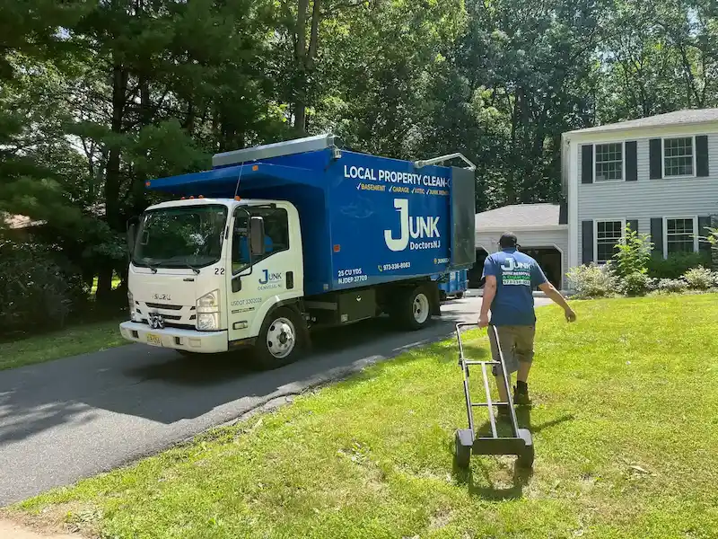 A JunkDoctors team member walking toward a residential garage with a heavy-duty dolly, ready to load one of our 25-cubic-yard trucks during a New Jersey garage cleanout.
