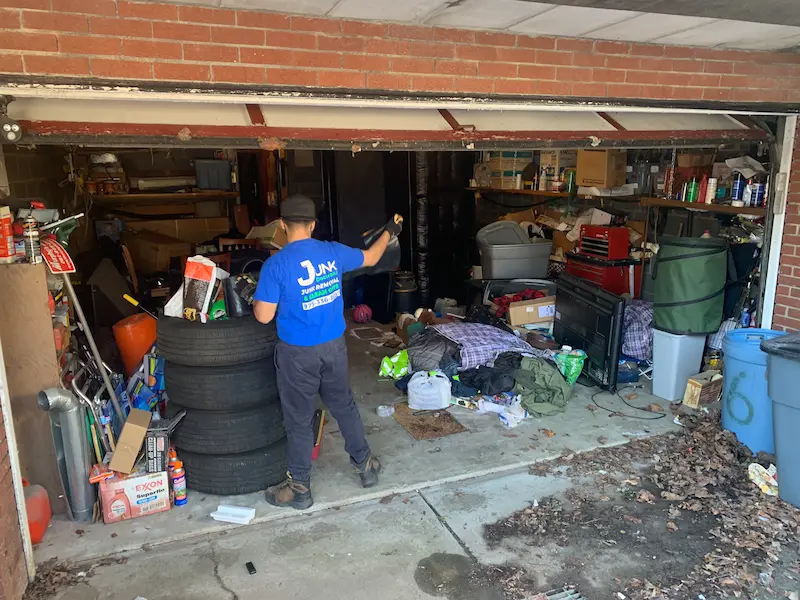 A JunkDoctors crew member clearing out a cluttered garage in New Jersey, including old tires, electronics, and household debris.