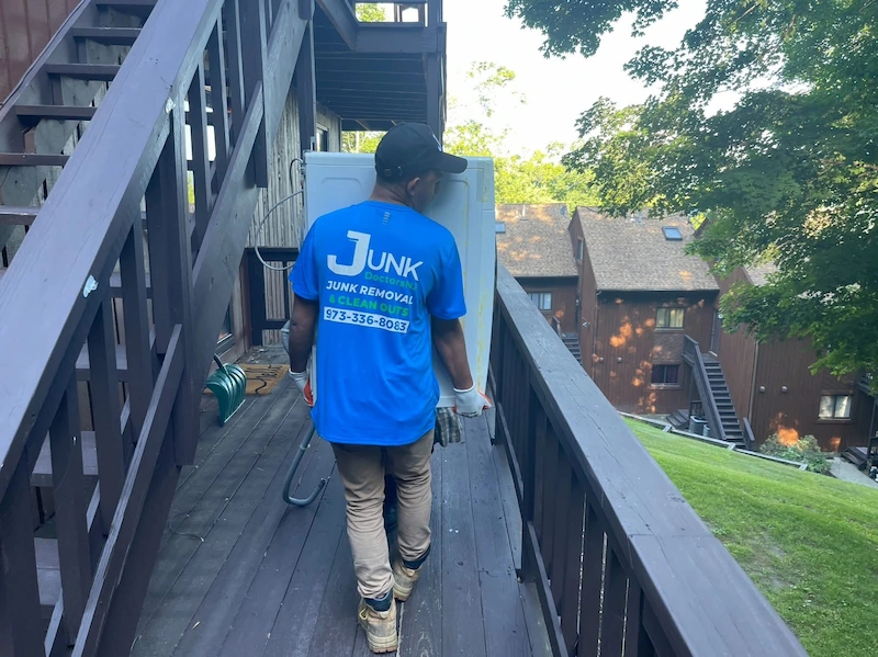 Professional junk removal team member hauling a large household appliance from a multi-level home in New Jersey.