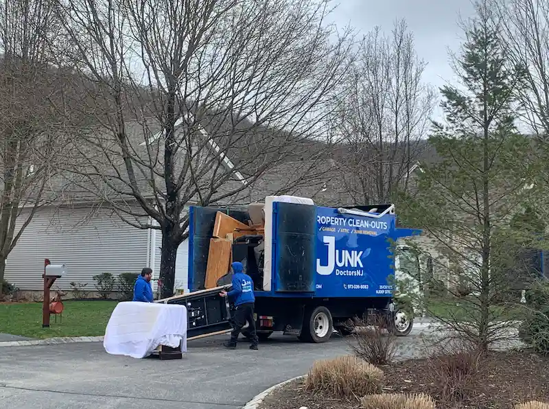 Professional JunkDoctors team members safely loading a bulky wooden dresser and heavy furniture into a 25-yard truck in New Jersey.
