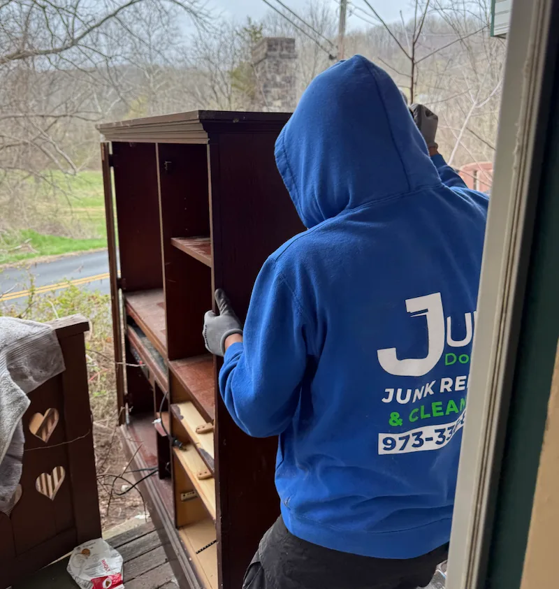 Junk Doctors NJ team member moving a heavy wood armoire out of a residential home for household junk removal and furniture disposal.