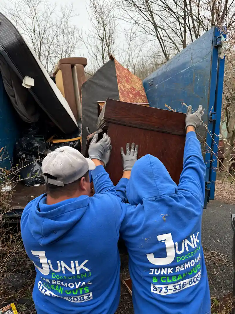 Junk Doctors NJ crew members loading heavy wooden furniture and mattresses into a truck during a residential household junk removal project in North NJ.