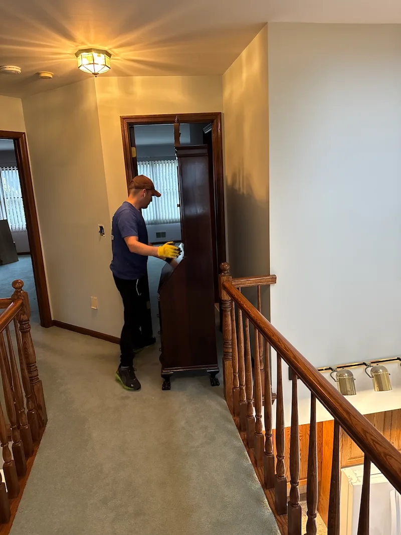 A JunkDoctors professional carefully moving a tall wooden secretary desk out of a bedroom hallway during an indoor furniture removal service in New Jersey.