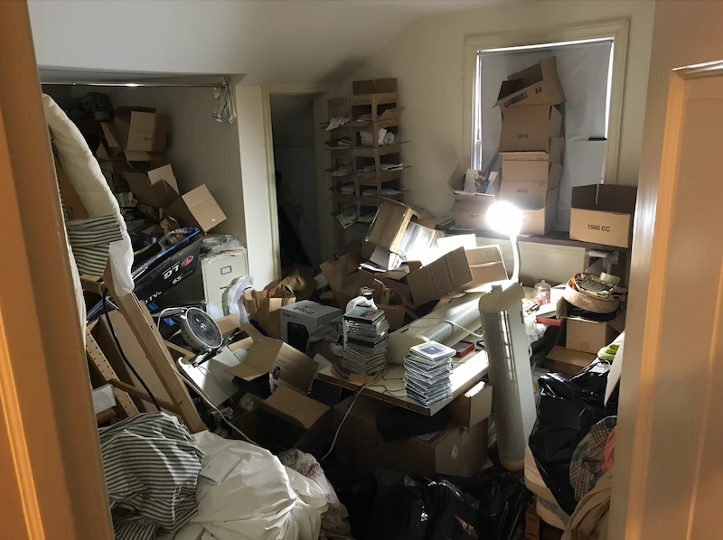 Overwhelmed room filled with boxes, loose paper, and household clutter before an emergency junk removal service.