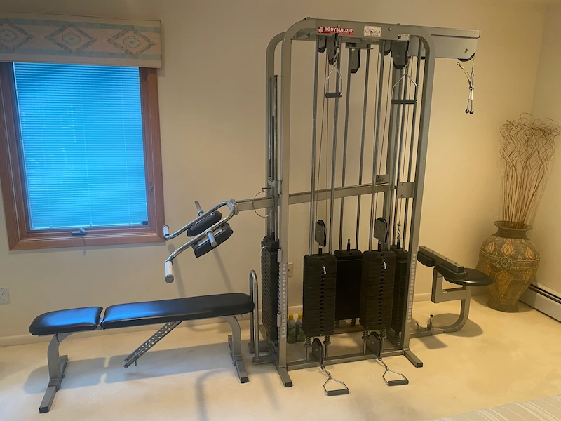 Large multi-station weight machine and bench press in a residential room before disassembly and removal by JunkDoctors NJ.
