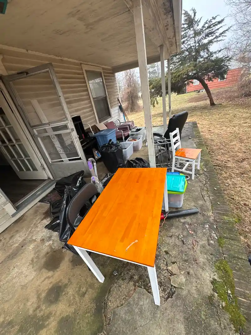 A cluttered residential porch in New Jersey filled with abandoned furniture and trash bags before JunkDoctors arrived for an eviction cleanout.