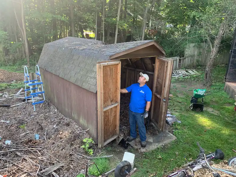 JunkDoctors NJ professional assessing a rotting, dilapidated wooden shed in a residential backyard before performing a full demolition and removal service.
