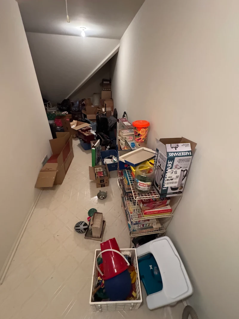 A first-person perspective looking down a narrow, deeply cluttered residential attic in New Jersey.
