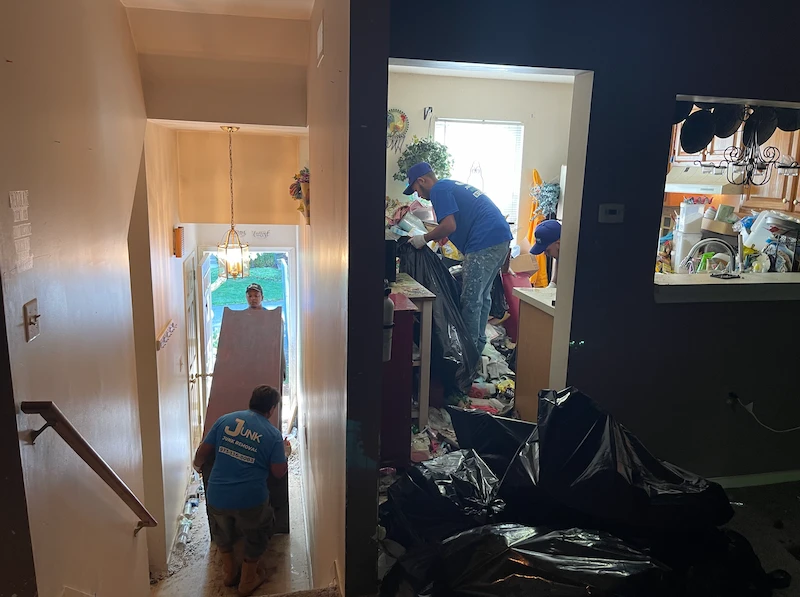 Professional junk removal team bagging trash and hauling abandoned furniture down stairs during an eviction cleanout in NJ.
