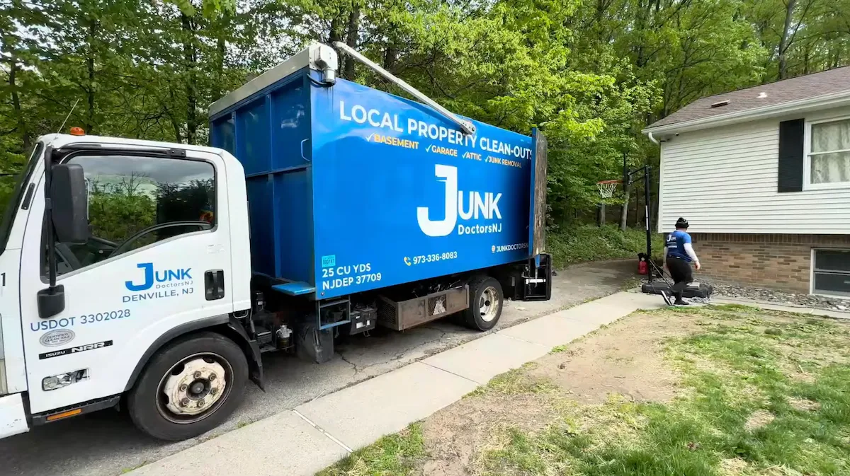 Junk Doctors NJ hauling truck parked in a residential driveway while a uniformed crew member performs a yard cleanup and exterior junk removal service.