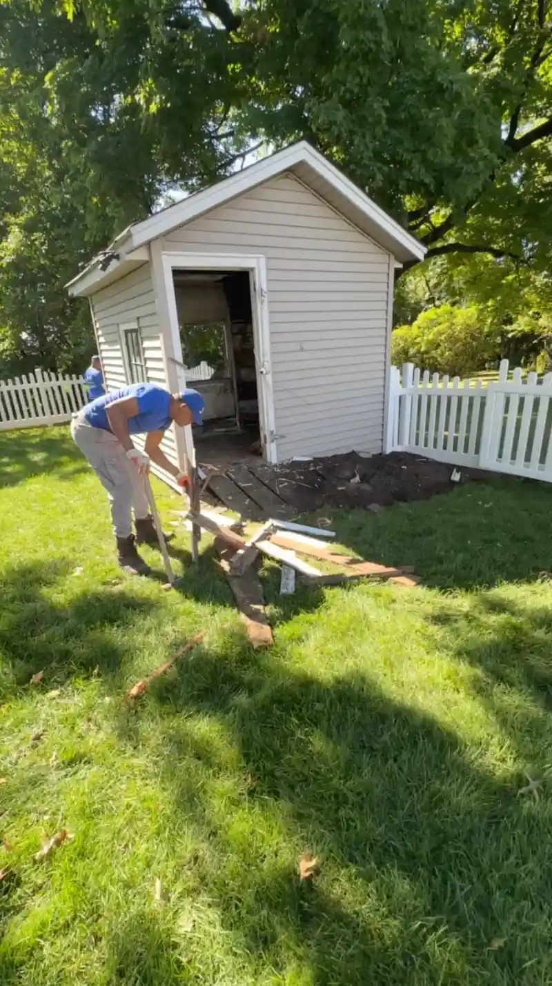 JunkDoctors crew member using a pry bar to dismantle a wooden backyard shed during a full demolition in New Jersey.