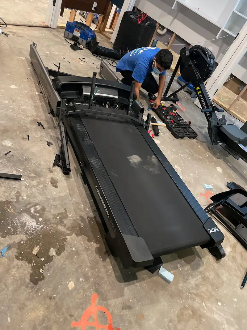 Junk Doctors NJ team using professional tools to disassemble a large NordicTrack treadmill for removal from a home gym in North NJ.