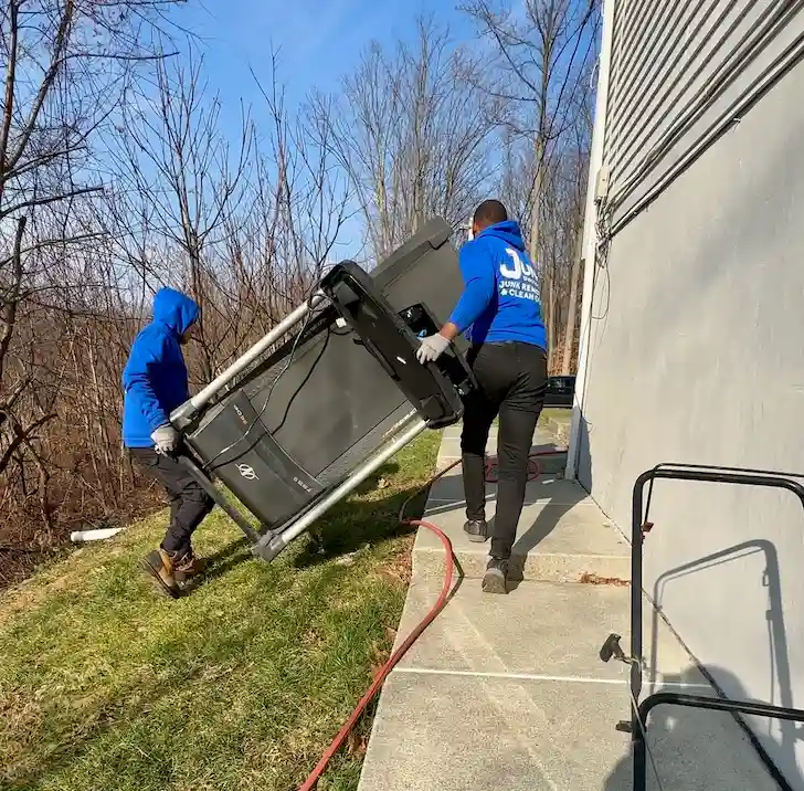 Junk Doctors NJ team carefully hauling a heavy treadmill out of a residential home for disposal.