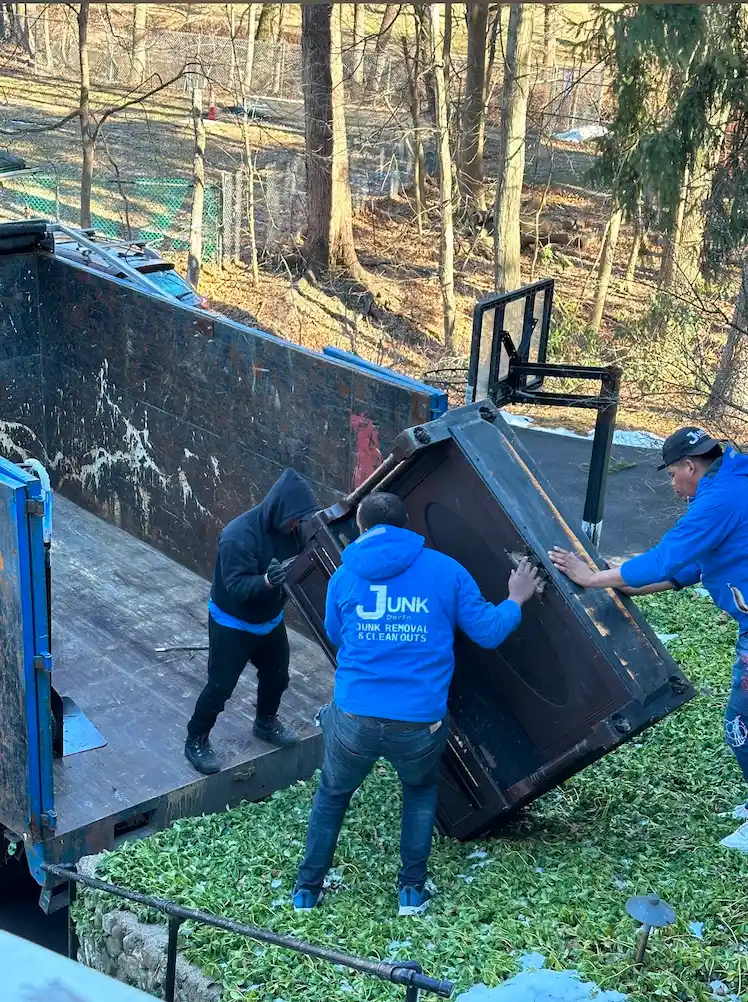 Three JunkDoctors crew members using coordinated strength to safely load a heavy upright piano into a junk removal truck during a residential cleanout in New Jersey.