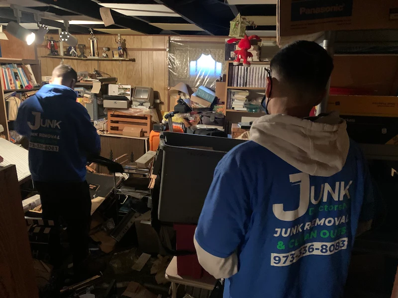 JunkDoctors NJ team in a basement removing water-damaged books, shelving, and household debris after a flood.