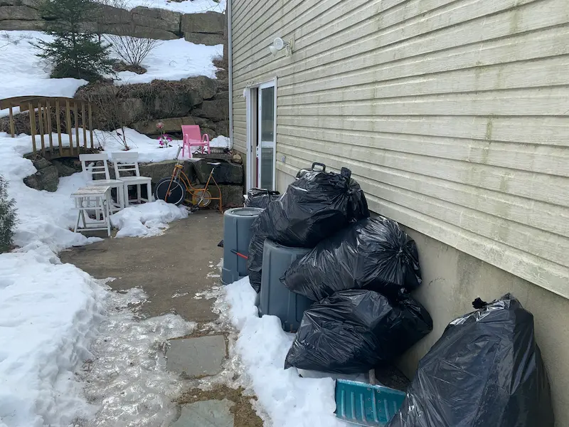 Junk Doctors NJ performing a winter yard cleanup with trash bags, old chairs, and a bicycle being removed from a snowy patio.