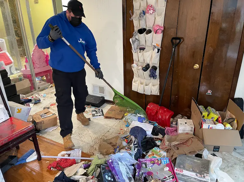 JunkDoctors team member clearing heavy floor clutter and loose debris during a residential hoarding cleanout.
