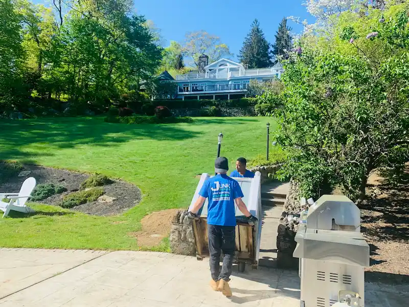 A JunkDoctors crew safely moving a heavy item down a stone walkway of a large luxury estate in New Jersey during a full property cleanout.